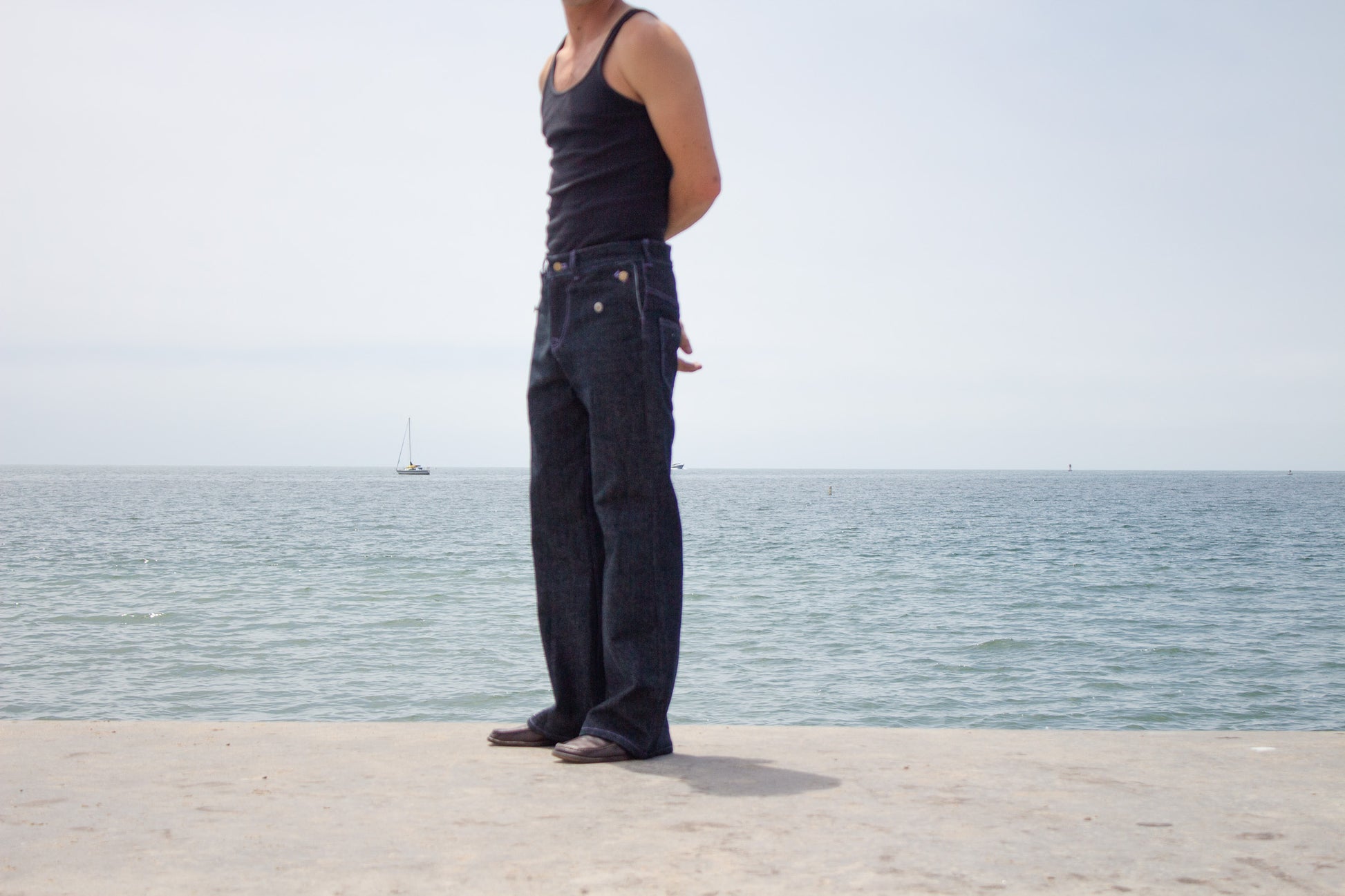 Person wearing flared jeans and a tank top standing on a dock with water in the background.