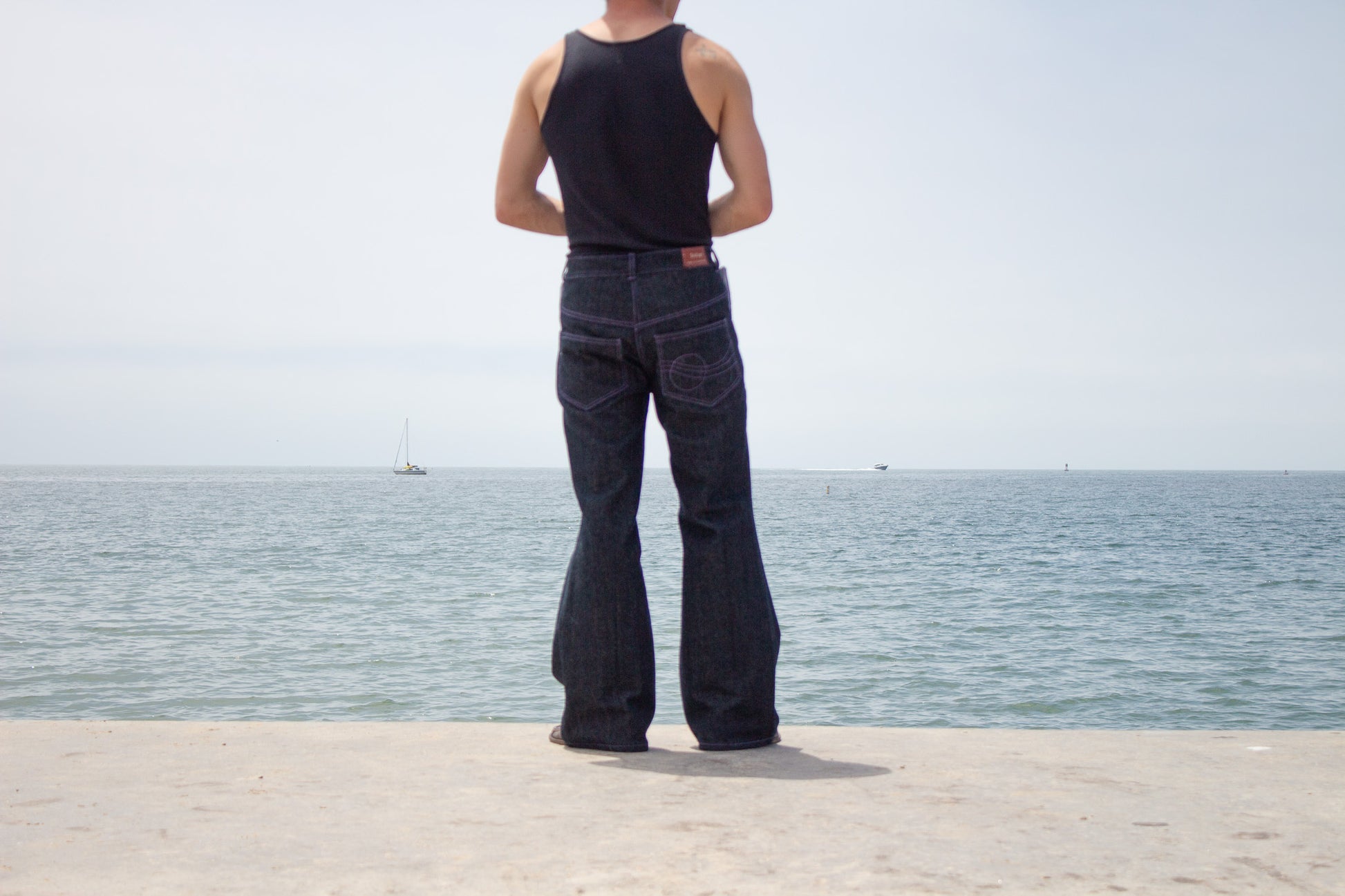 Person wearing black sleeveless top and dark jeans standing by a body of water.